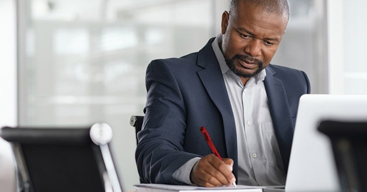 man sits at desk and writes notes