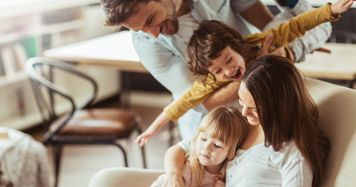 Man and wife and two kids laughing on sofa