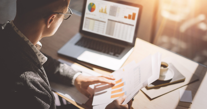 Man at desk reviewing graphs and charts on a laptop