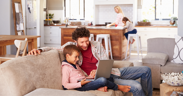 father and son sit on couch and use laptop computer